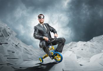 Odd businessman riding a small bicycle against paper background