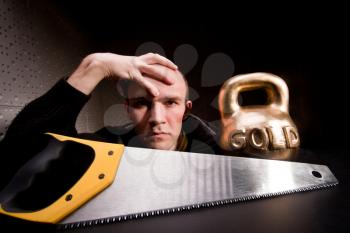 Thoughtful man with saw and heavy weight of gold