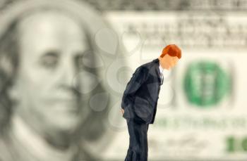 Miniature figurine of loser businessman with $100 banknote on background