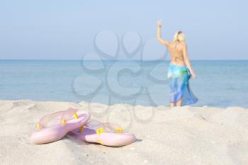 Flip flops on the beach with going for a swim woman on background