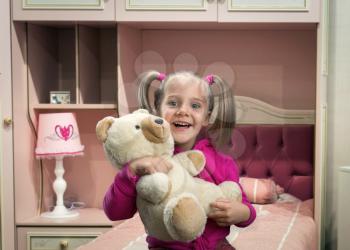 Funny girl holding toy bear at her cozy room