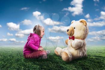 Small cute girl sits and looks at toy bear on nature background