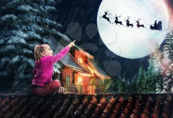 Girl sits on the roof in The Christmas eve pointing to the deer in the sky