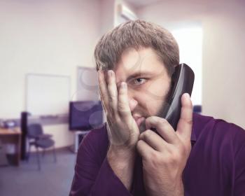 Frustrated man speaks on the phone in the office