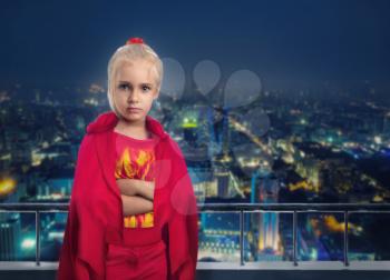 Serious little girl in super hero costume against the night city