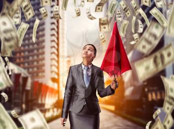 Businesswoman with red umbrella looks at money falling