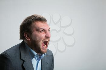 Young angry businessman shouting over grey