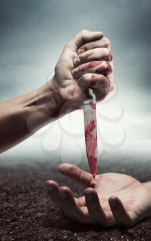 Bloody human hand with knife under another hand