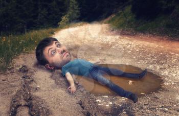 Man with a huge head in the puddle on rut road after rain in forest