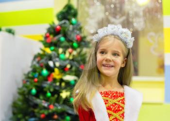 Happy little girl against holiday tree at Christmas party