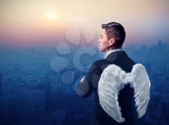 Businessman with angel wings on his back looking at sunrise over city