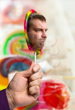 Male hand holding a lollipop with male face in candy store