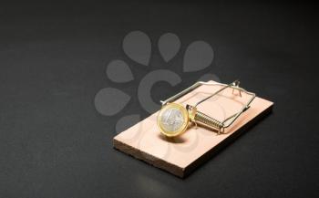 A gold coin in the mouse-trap on a grey table