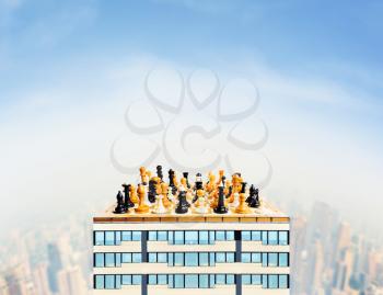 Board with chess figures on the top of the skyscraper against the city