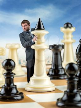 Businessman hiding behind black king on the chess board 