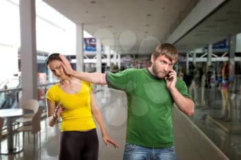 Bearded man talking by mobile phone pushes aside his wife in the shopping mall