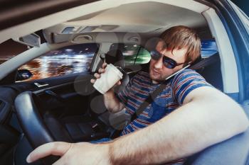Man speaking on the phone in the car and drinking coffee