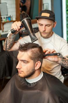 Young man having hair dress, barber working with hair dryer