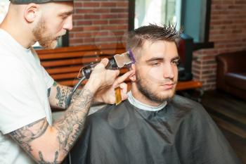 Side view of a young man having hair dress, barber working with hair clipper
