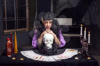 Sorceress practises witchcraft with pack of cards leaning on the skull