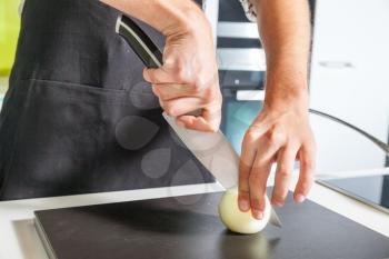 Close up of man's hands slicing onion on the board