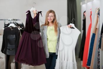 Young woman choosing which dress to buy