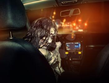 The undead girl with bloody face rides in the car agaist night city on the background. Scary. Halloween.