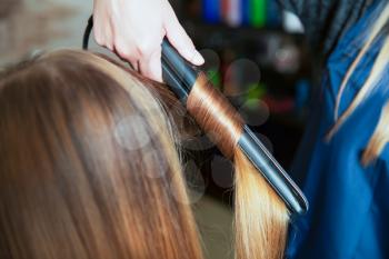 Woman hairdresser making hairstyle using professional equipment for long hair of young female in beauty salon. 