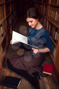 Student girl with open book reading it in university library.