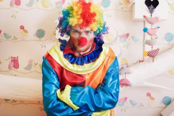 Portrait of angry clown with rainbow colored hairstyle and makeup. Decorative nesting box with input in form of heart on the background.