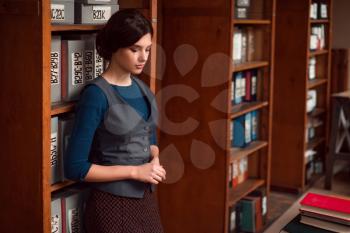 Female student standing with eyes closed in college library. Bookshelf with books and textbooks on the background.