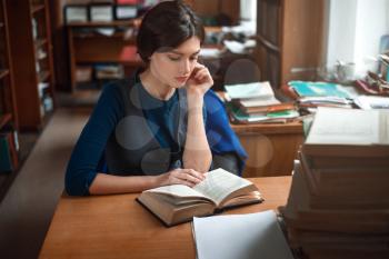 Portrait of clever student reading a book in university library.