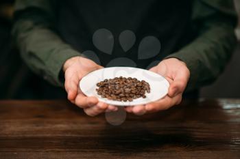 Male hands holds white plate with grain of coffee. Fresh coffee aroma.