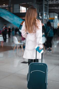 Young female traveller walking the airport hall draging suitcase. Blured airport cafe on the background