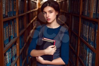 Student girl or woman with books between bookshelves in library. 