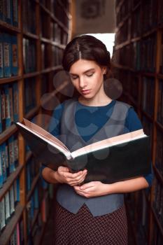 Portrait of serious student with open book reading it in college library.