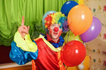 Funny clown with a bunch of colorful air balloons standing in the room.