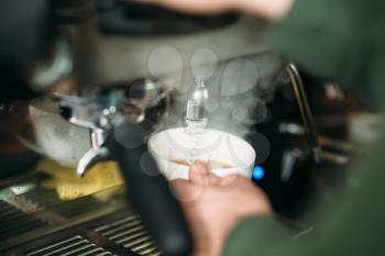 Focused male hands with white cup and blured coffee machine. 