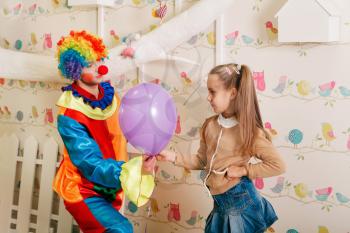 Birthday entertainment with clown in colourful costume. White tree and nesting boxes on the background.