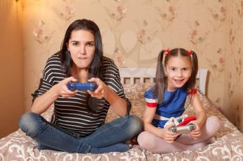 Young mother and her little daughter plays game console.