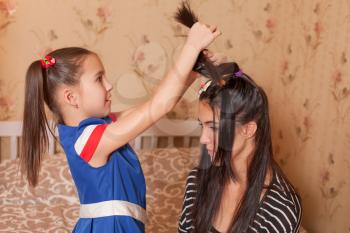 Female child playing hairdresser with her young mother.