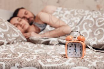 Alarm clock  with embracing young couple sleeping in bed on background.