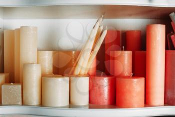 Wax candle collection on white wooden shelf closeup.