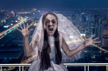 Screaming zombie bride, night city on background. Disheveled woman with tear-stained face in wedding dress and white veil