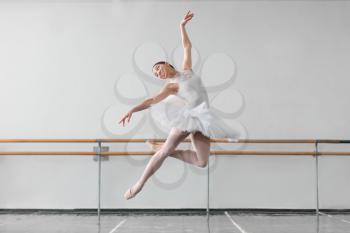 Beautiful female ballet dancer keep the rack in ballet class, barre and white wall on background