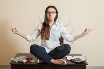 Female accountant sitting in yoga pose on the table in office