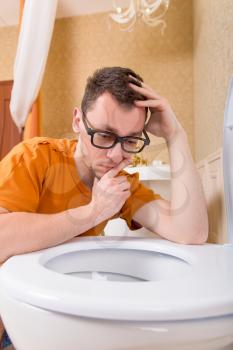 Thoughtful man in glasses looking into the toilet bowl. Luxury bathroom interior on background