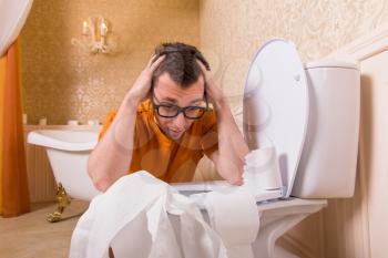 Man in glasses sits resting his hands on the toilet. Bathroom interior in vintage style on background