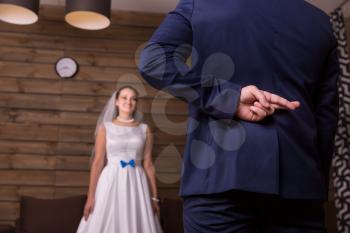 Groom with crosses fingers makes the promise to bride, wooden background.