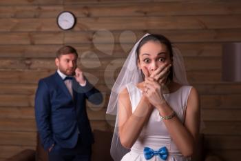 Surprised bride against groom talking on the phone, wooden room on background.